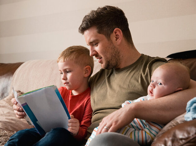 Photo of a father reading with his son and young baby